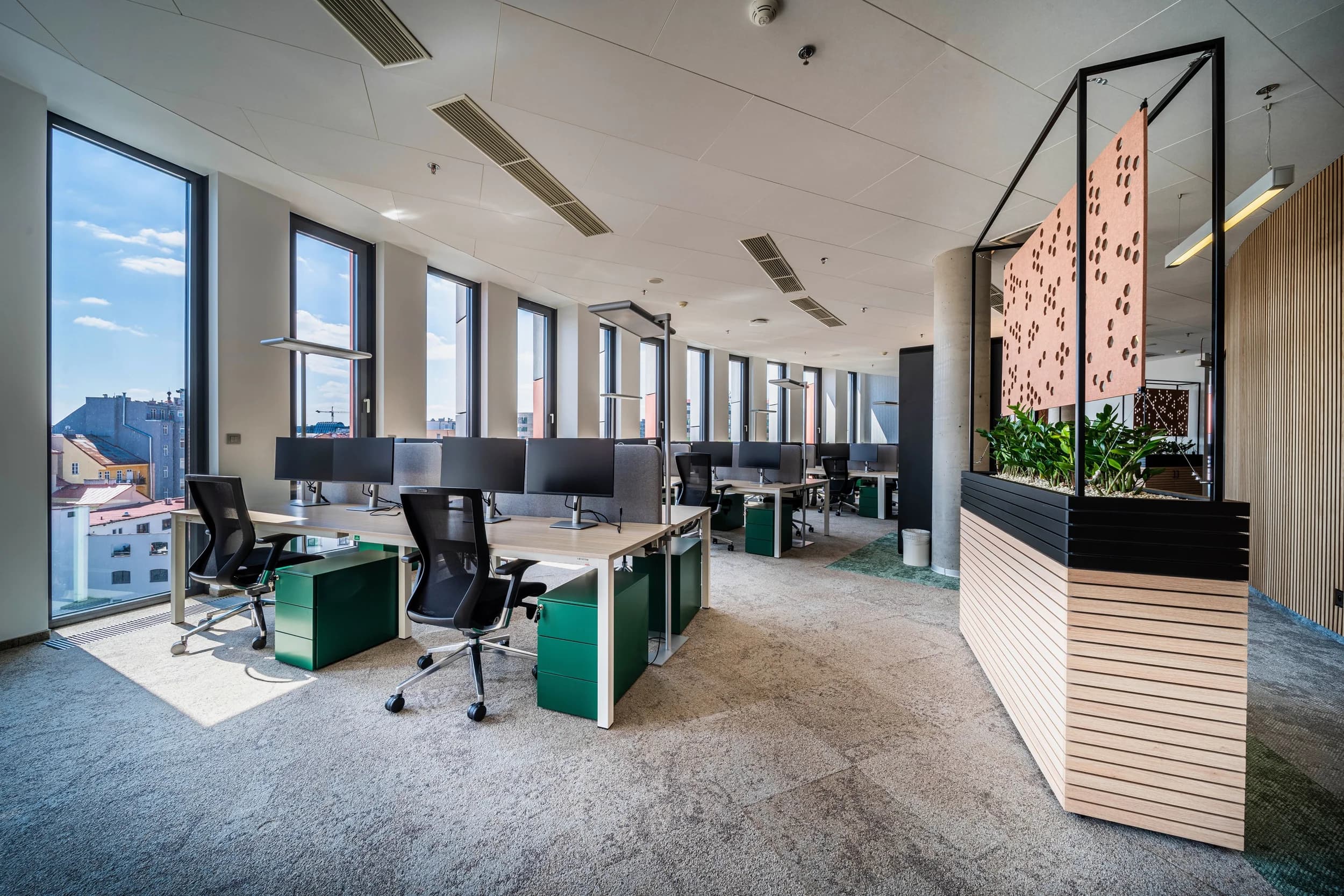 Open space Kooperativy v Praze s pracovními stoly, zelenými kontejnery a dřevěným truhlíkem jako předělem