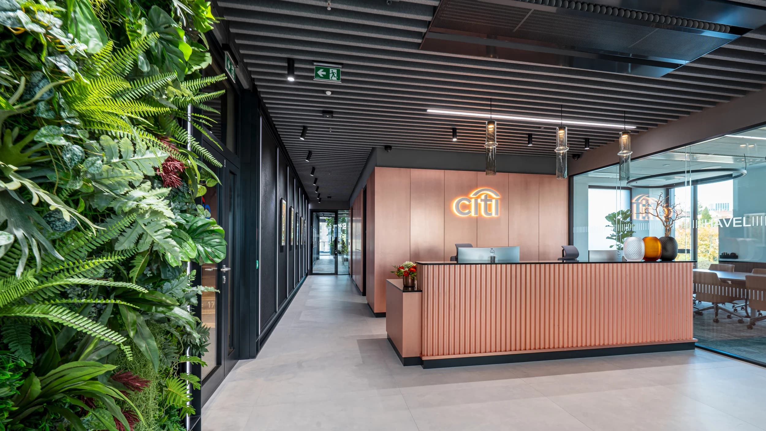 Recepce Citibank v Praze s měděným pultem, podsvíceným logem a zelenou stěnou z rostlin